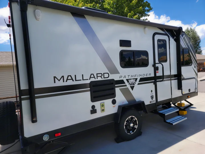 A white Mallard Pathfinder travel trailer, perfect for an RV rental, sits on a paved lot under a blue sky.. Heartland RVs Mallard Pathfinder 2022