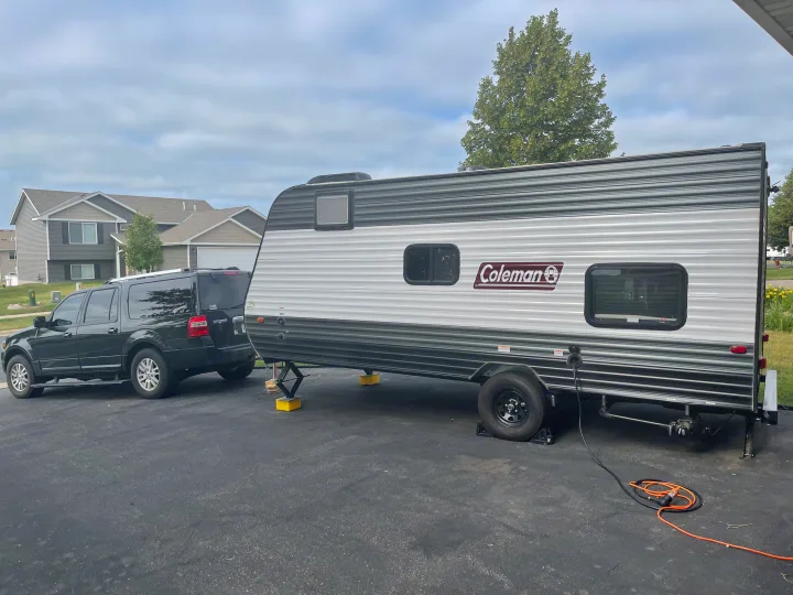 An RV rental Coleman travel trailer is parked, stabilized, and connected to power beside an SUV on a paved driveway.. Dutchmen Coleman Lantern LT 2021