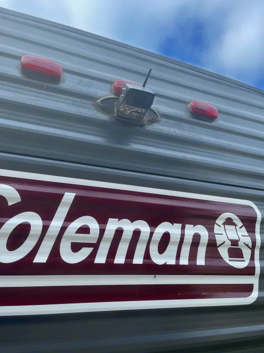 Exterior of a Coleman RV rental, showing its corrugated grey siding, a backup camera, and red marker lights.. Dutchmen Coleman Lantern LT 2021