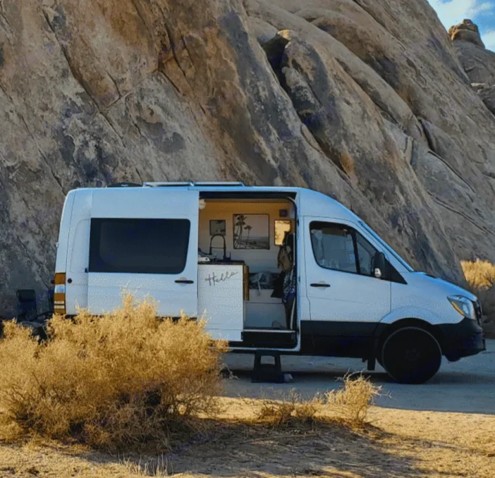 White camper van RV rental parked in a rocky desert landscape. Side door open, revealing a cozy interior for outdoor adventures.. Mercedes-Benz Sprinter RV Motorhome Campervan 2016