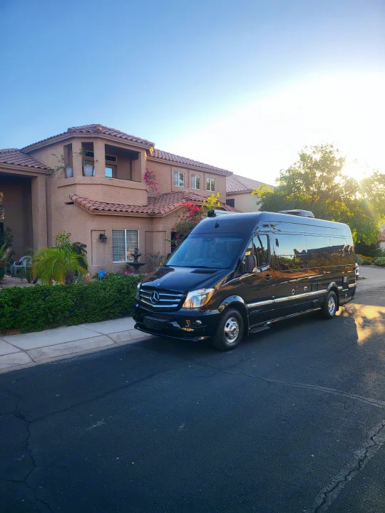 A black Mercedes-Benz Sprinter Airstream RV rental is parked on a residential street next to a beige house, on a sunny day.. Airstream Interstate 2016