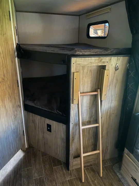 RV rental interior with two cozy bunk beds and a ladder for top bunk access, featuring light wood-grain finishes.. Forest River Cherokee Alpha Wolf 2021