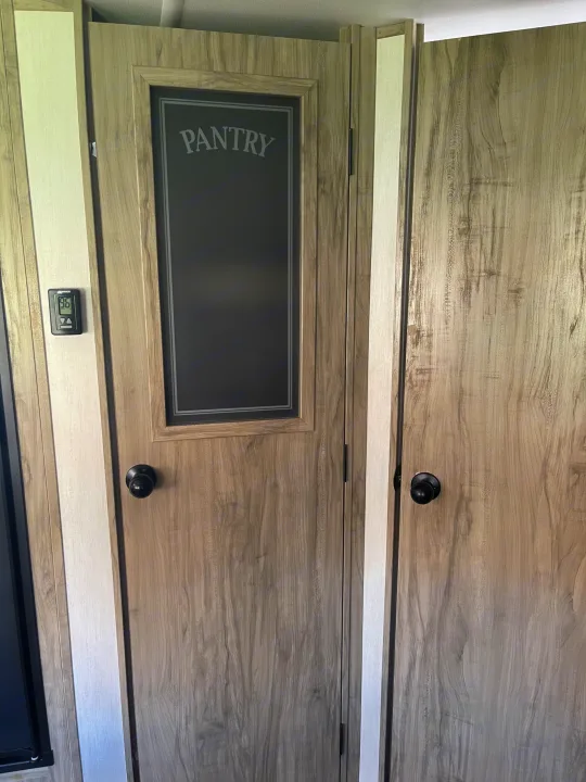RV rental interior: A wooden "Pantry" door, adjacent storage door, and thermostat for compact living.. Forest River Cherokee Alpha Wolf 2021