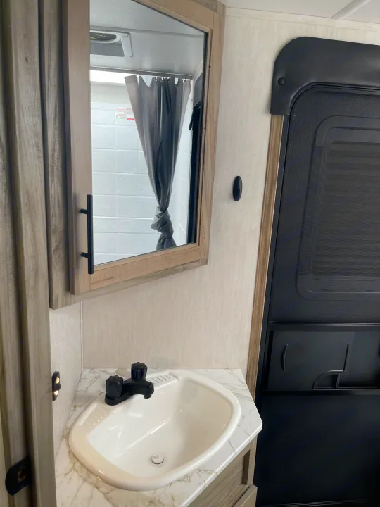 **RV rental** bathroom: compact vanity with sink & mirror reflecting shower, beside an entrance door.. Forest River Cherokee Alpha Wolf 2021