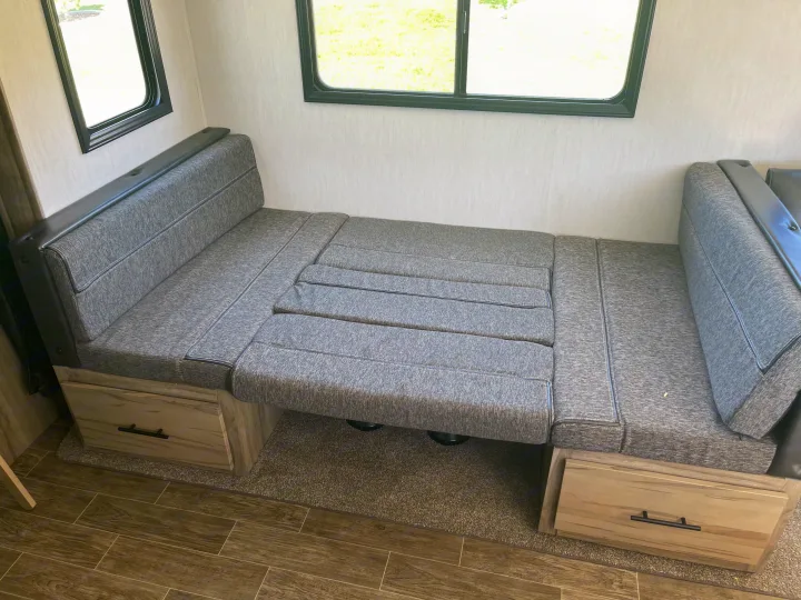 Cozy RV rental interior: grey dinette cushions transform into a bed, with storage drawers and large windows for light.. Forest River Cherokee Alpha Wolf 2021