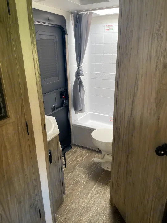 This RV rental bathroom offers a compact shower, toilet, and vanity sink with wood-look flooring.. Forest River Cherokee Alpha Wolf 2021