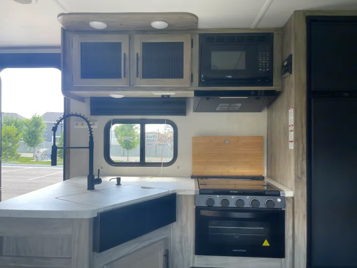 Clean, modern kitchen in an RV rental, featuring a sink, stove, microwave, and fridge.. Forest River Cherokee Alpha Wolf 2021