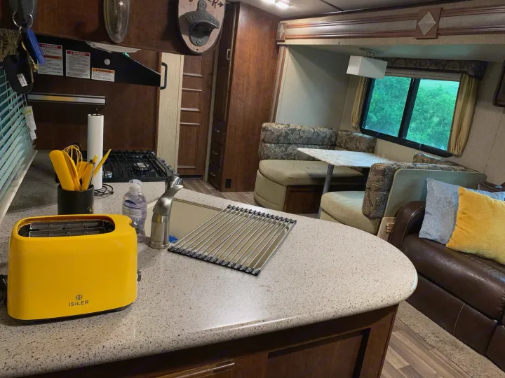 Explore this RV rental's functional kitchen with a yellow toaster, sink, and cozy dinette, showcasing a practical travel setup.. Other Outback 2017