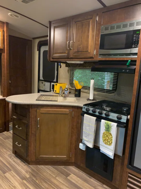 Modern RV rental kitchen featuring an island, wood cabinets, stove, and microwave. Perfect for travel cooking.. Other Outback 2017