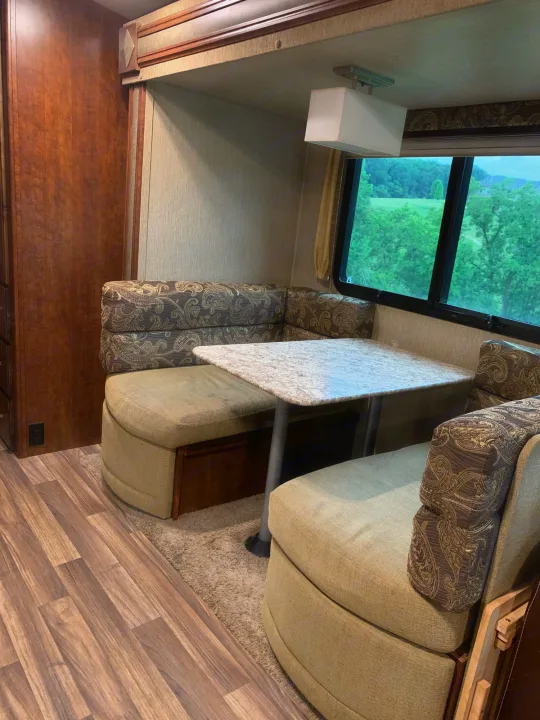 Inside an RV rental: a well-appointed dinette with patterned bench seating, a light-colored table, and a large window view.. Other Outback 2017