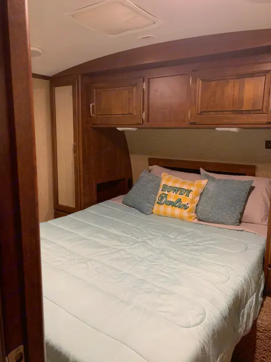 Cozy RV rental bedroom: light blue bedding, 'Howdy Darlin'' pillow, dark wood cabinets, and mirrored closet.. Other Outback 2017