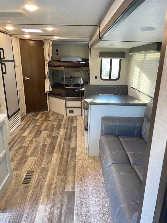 Explore this cozy RV rental interior! Features include bunk beds, a dinette with table, a sofa, and wood flooring.. Keystone Bullet 2020