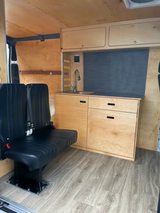 Modern RV rental interior with light wood paneling, a functional kitchenette, and passenger seats for adventure.. RAM ProMaster 2022