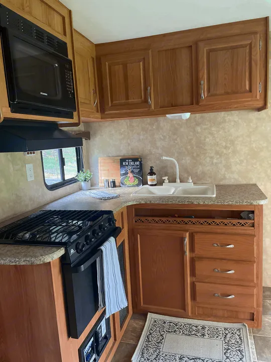 Compact and functional kitchen in an RV rental, featuring a Sylvania microwave, gas stove, double sink, and wood cabinets.. Jayco Jay Flight 2009