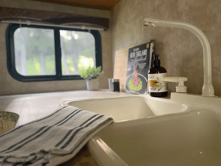 RV rental kitchen: a bright, functional space with a sink, faucet, soap, 'New England Cookbook,' and a window overlooking greenery.. Jayco Jay Flight 2009