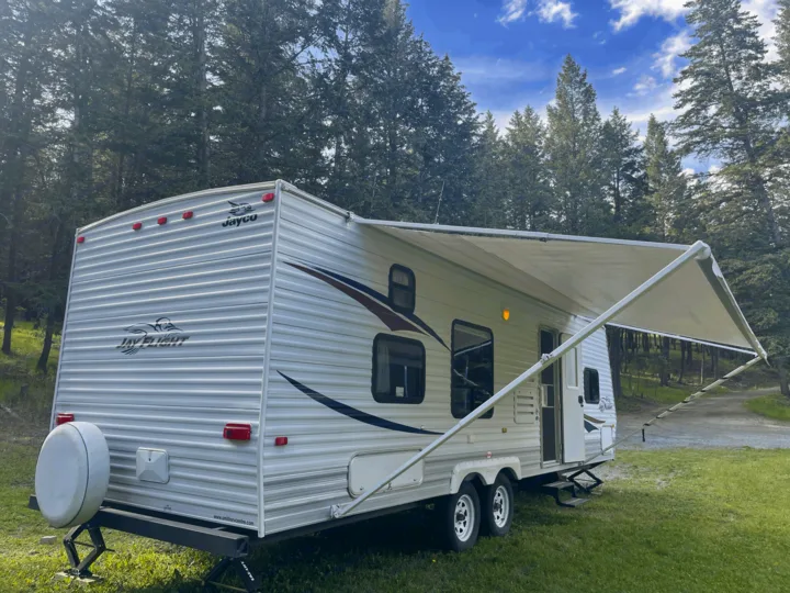 Jayco travel trailer with awning extended, parked at a grassy campsite among tall trees. Great for your next RV rental.. Jayco Jay Flight 2009