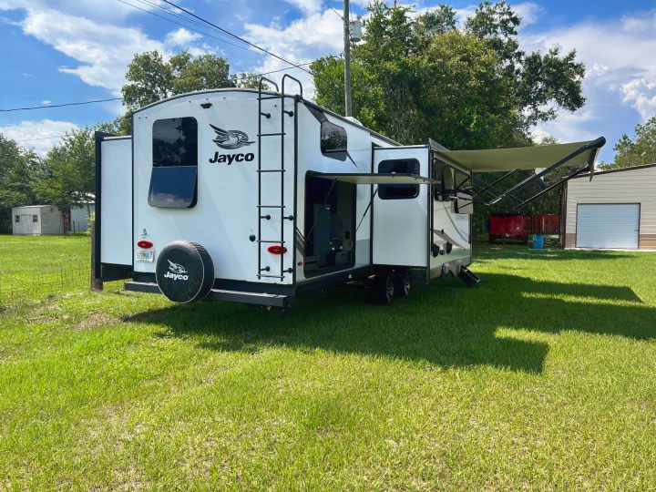 White Jayco travel trailer RV rental set up on grass, awning extended for shade. Perfect for adventures.. Jayco White Hawk 2022