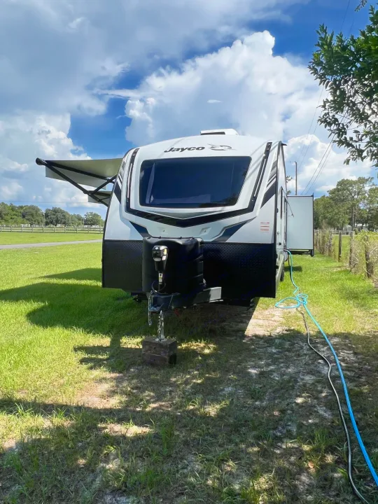 Experience RV rental freedom! White Jayco travel trailer with awning extended, parked in a sunny field.. Jayco White Hawk 2022