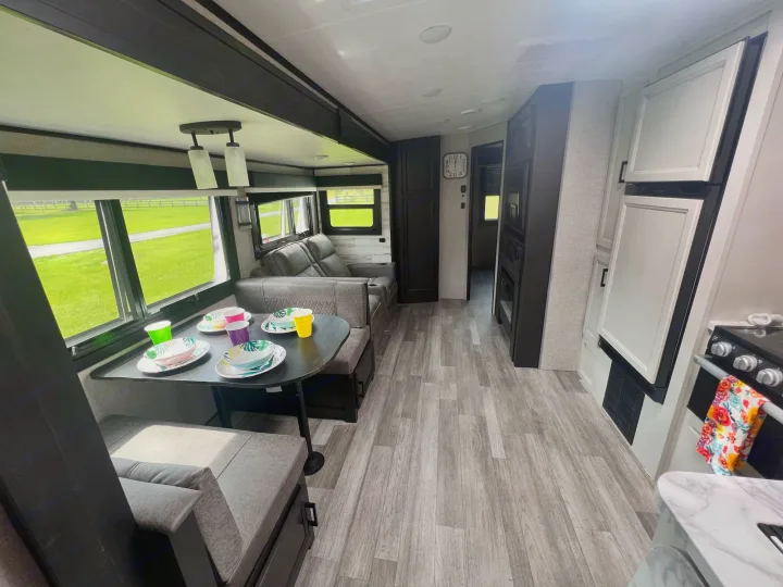 Step inside this RV rental's spacious living and dining area, featuring a sofa, table, kitchen, and large windows for travel views.. Jayco White Hawk 2022