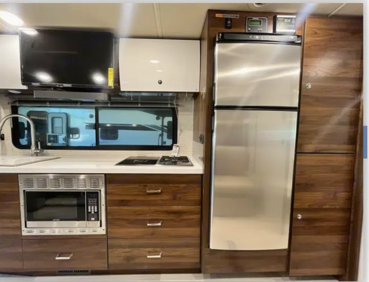Modern RV rental kitchen featuring a sink, stove, microwave, fridge, and TV for compact travel.. Winnebago View 2022