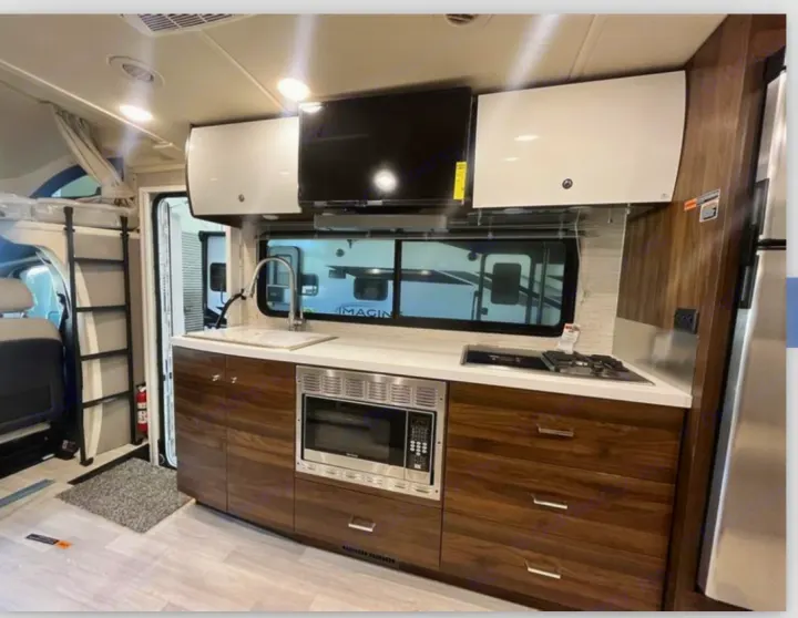 Compact RV rental kitchen features: sink, microwave, stovetop, TV, and bunk ladder. Ideal for mobile living.. Winnebago View 2022