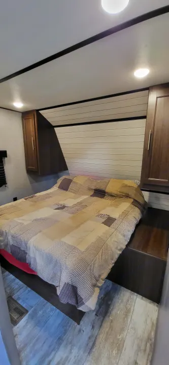 RV rental bedroom showcasing a patterned bedspread, overhead cabinets, and wood-look flooring. Bright and inviting.. Crossroads RV Zinger Lite 2020