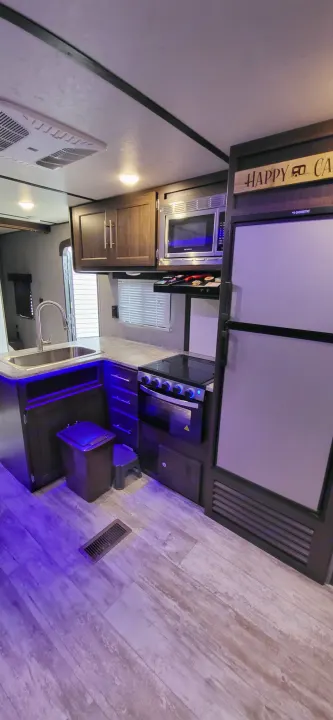 Experience comfort in this RV rental kitchen, featuring a fridge, microwave, oven, sink, wood-look flooring, and purple accent lighting.. Crossroads RV Zinger Lite 2020