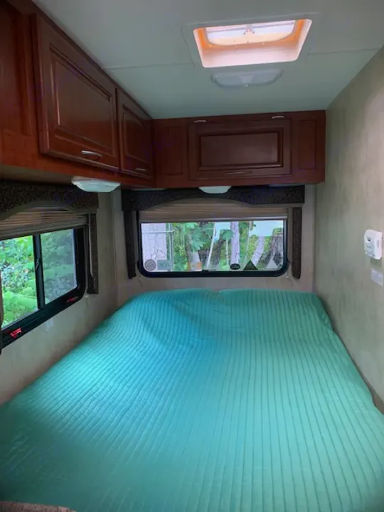 An RV rental's interior: A compact living space featuring a turquoise quilted bed, wooden cabinetry, and windows.. Four Winds Four Winds Motorhome 2011