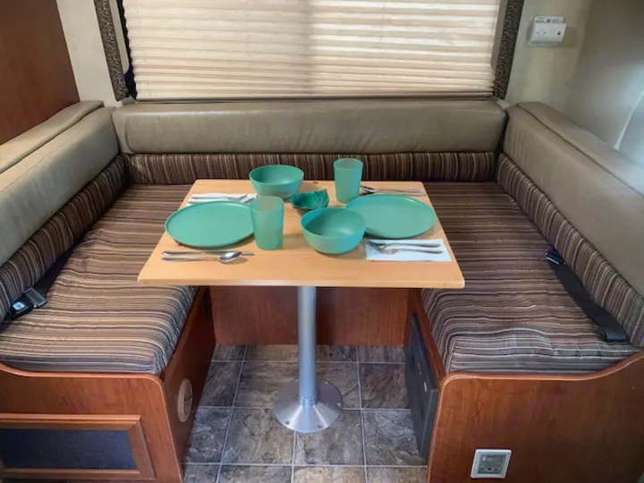 RV rental interior: U-shaped dinette with striped cushions and a table set for two with teal dishes.. Four Winds Four Winds Motorhome 2011