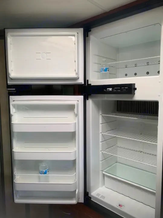 Inside an empty RV rental refrigerator. All doors and lower drawers are open, revealing clear shelves and a few water bottles.. Four Winds Four Winds Motorhome 2011