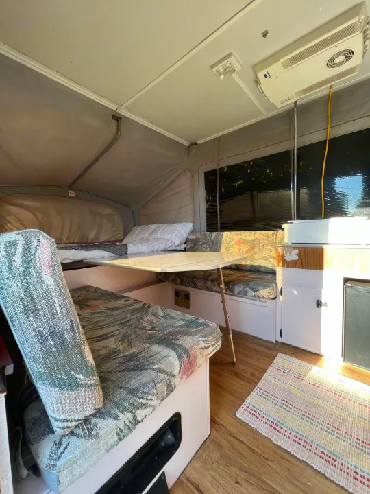 Cozy pop-up RV rental interior with bed, dinette, and kitchen. AC unit overhead.. Jayco Eagle 1996
