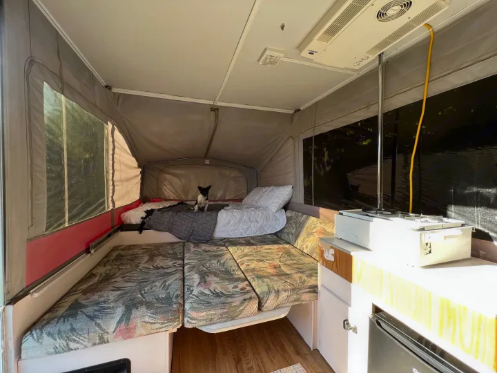 Pop-up RV rental interior: features comfy beds, seating, a compact kitchen with a stove, and a small dog on the bed.. Jayco Eagle 1996