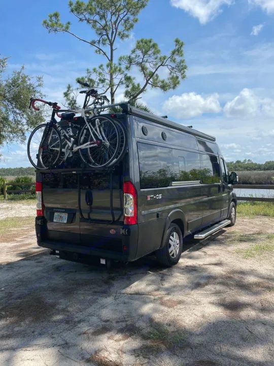 This black RV rental, a camper van with bikes on the rear, is parked outdoors, ready for adventure.. Entegra Coach Ethos 2021
