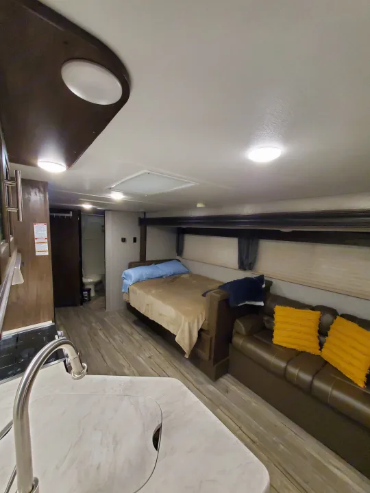 Compact RV rental living space: kitchen sink, sofa with yellow pillows, bed, and visible bathroom. Bright and ready for travel.. Forest River Cherokee Grey Wolf 2018