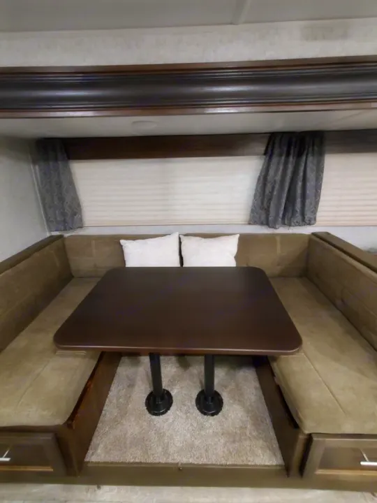 RV rental dinette featuring U-shaped brown seating, a dark table, and window blinds. Ideal for relaxing or dining inside.. Forest River Cherokee Grey Wolf 2018