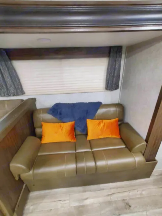 Comfortable RV rental living area featuring a brown couch, orange pillows, and a window with blinds.. Forest River Cherokee Grey Wolf 2018