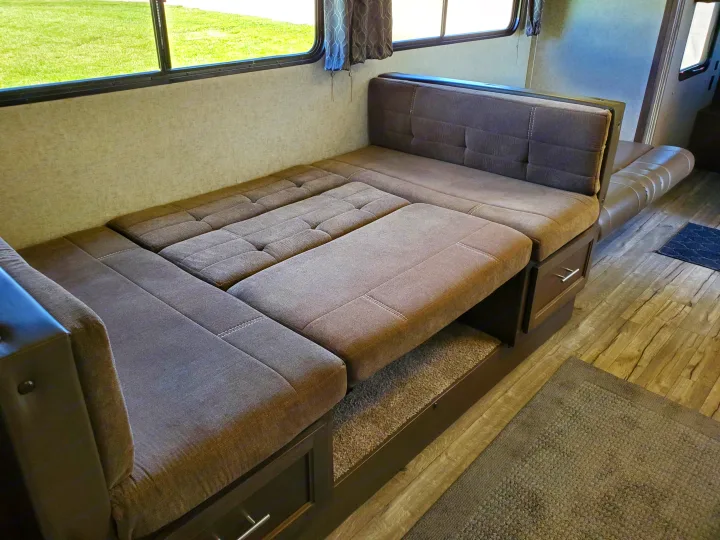 This RV rental features a versatile U-shaped dinette with brown cushions, easily converting into a comfortable bed for guests. Storage drawers below.. Forest River Cherokee Grey Wolf 2018