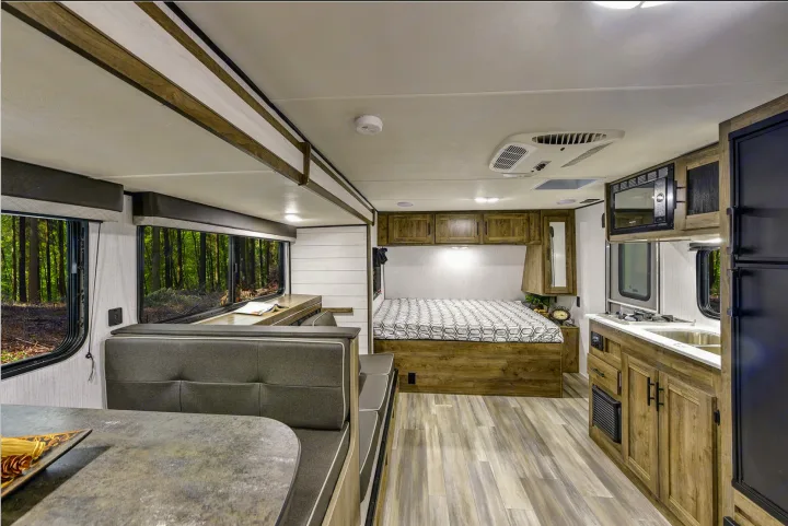 This modern RV rental interior features a kitchen, dining area, bedroom, and large windows with forest views.. Heartland RVs Pioneer Trail Blazer 2022
