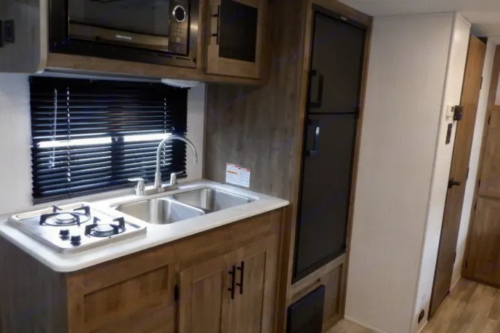 RV rental kitchen with a two-burner stove, double sink, microwave, and refrigerator, ready for your road trips.. Heartland RVs Pioneer Trail Blazer 2022