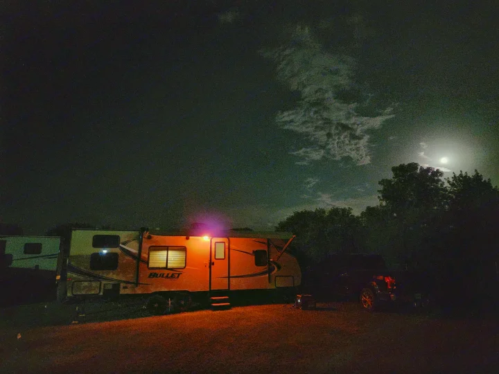 An RV rental glowing orange at night under a bright moon and clouds, with a truck nearby. Perfect for a cozy camping trip.. Keystone Bullet 2017