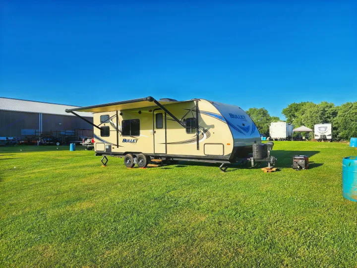 Spacious Bullet Crossfire RV rental parked in a sunny green field. Features an extended awning and generator for camping.. Keystone Bullet 2017