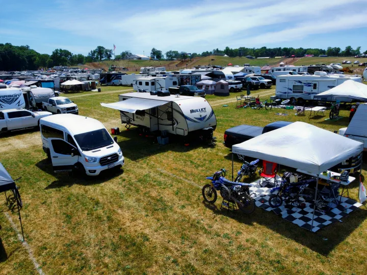 An aerial view shows RVs, tents, and dirt bikes parked on grass at a sunny outdoor event, ideal for an RV rental trip.. Keystone Bullet 2017