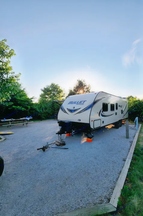 Bullet Crossfire RV rental on a gravel campsite. Golden hour light illuminates the setting, with a picnic table.. Keystone Bullet 2017