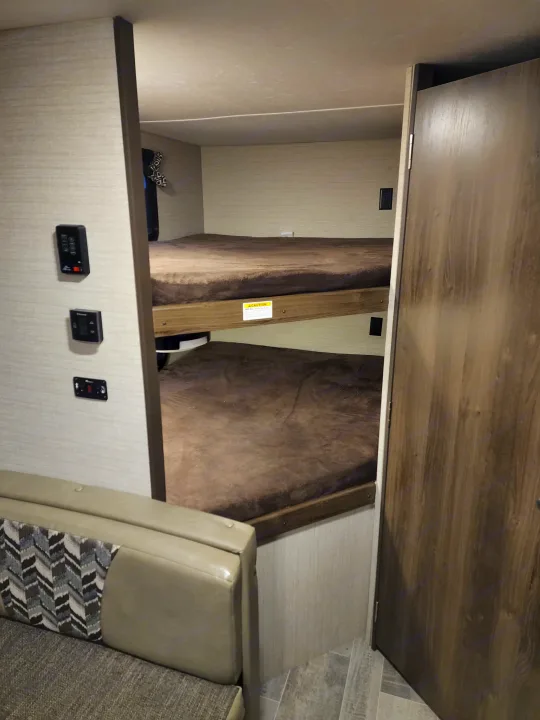 RV rental interior with two bunk beds and a dinette seating area. Wall-mounted controls are visible near the light-colored sofa.. Keystone Bullet 2017