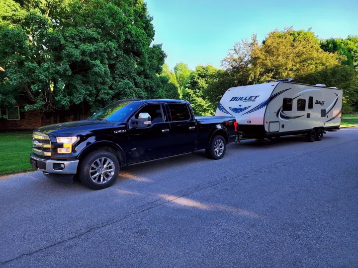 Black pickup truck towing a Bullet travel trailer on an asphalt road. Ready for an RV rental trip or camping adventure!. Keystone Bullet 2017