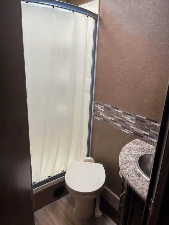RV rental bathroom features a compact toilet, frosted glass shower, and a small sink with a mosaic tiled backsplash. Functional space.. Thor Motor Coach Freedom Elite 2019