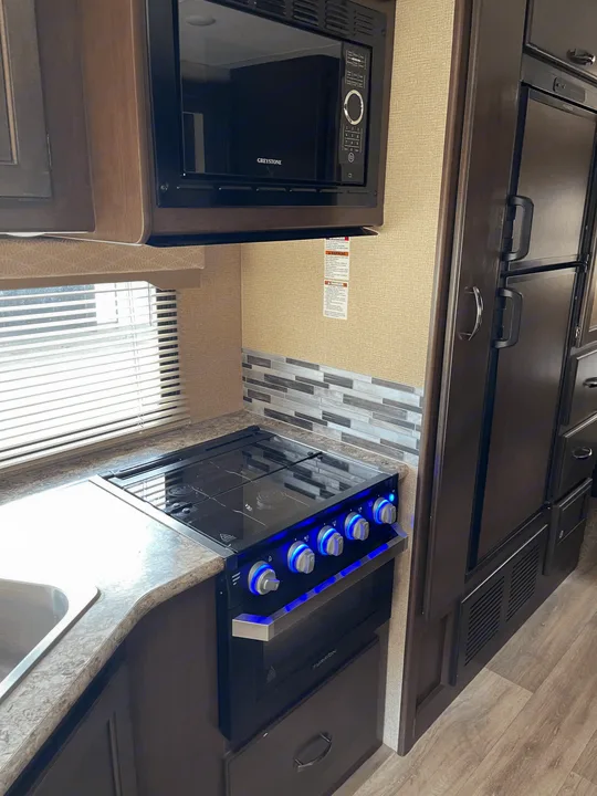 Modern RV rental kitchen with Greystone microwave, Furrion stove/oven, sink, and refrigerator. Fully equipped for trips!. Thor Motor Coach Freedom Elite 2019