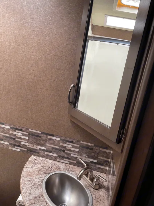 Compact rv rental bathroom with sink, patterned counter, tiled backsplash, and mirrored cabinet reflecting the RV interior.. Thor Motor Coach Freedom Elite 2019