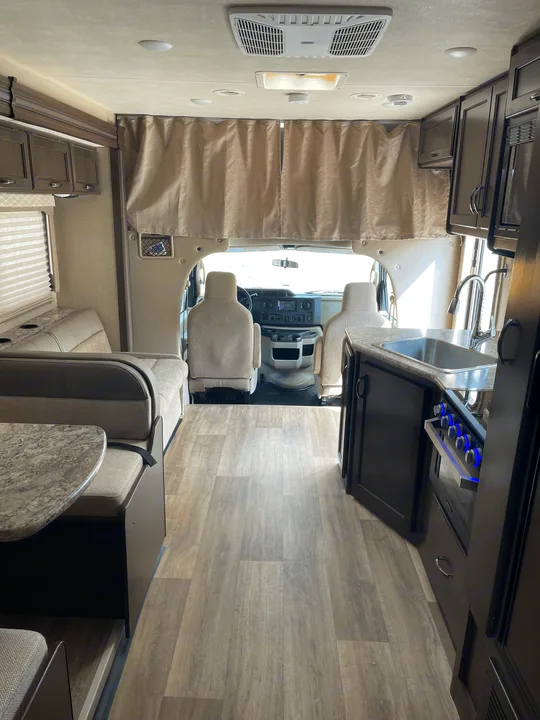 Clean rv rental interior, showing a full kitchen, comfortable dinette, and bright cockpit area ahead.. Thor Motor Coach Freedom Elite 2019