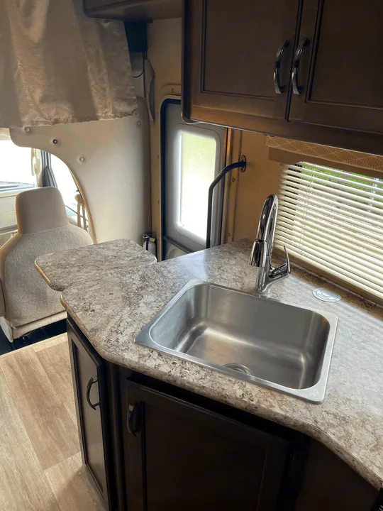 Explore this RV rental's kitchen: a bright, clean space featuring a stainless steel sink, modern faucet, ample cabinets, and front seating.. Thor Motor Coach Freedom Elite 2019